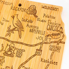 The Destination Illinois Cutting Board, a 16-1/2" x 9-1/4" piece from Totally Bamboo, is crafted with a bamboo surface featuring laser-engraved artwork of Illinois. It highlights cities such as Rockford, Waukegan, Chicago, Naperville, and Joliet, and includes illustrations of Route 55, a cardinal bird, and Starved Rock State Park.