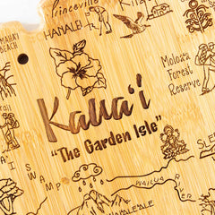 The Destination Kauai Cutting Board by Totally Bamboo, measuring 9-3/4" x 12-1/2", features intricate laser engravings of Kaua'i landmarks like "Hanalei," "Moloa'a Forest Reserve," and "Wailua River," complemented by a hibiscus flower, with the phrase "Kaua'i The Garden Isle" prominently displayed.