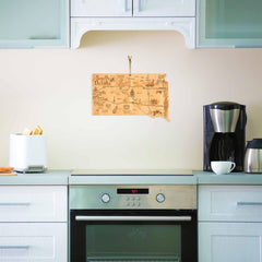 A modern kitchen with light gray cabinets showcases a stainless steel oven and a coffee maker on the counter. Hanging on the wall above the oven is the Totally Bamboo Destination South Dakota Cutting Board, which measures 9-3/4" x 16". Beside it, a toaster with bread slices is set for breakfast.