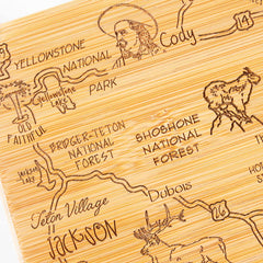 The Destination Wyoming Cutting Board by Totally Bamboo is a laser-engraved piece that beautifully illustrates a wooden map featuring the regions in and around Yellowstone National Park, highlighting attractions such as Yellowstone Lake, Old Faithful, Cody, Shoshone National Forest, Bridger-Teton National Forest, and Jackson. This state-shaped board measures 11" x 14-1/4" and includes detailed engravings of animals and landscapes.