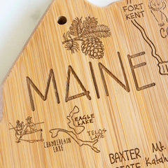 Discover the Totally Bamboo Destination Maine Cutting Board, measuring 15" x 10-1/2". This beautifully crafted bamboo board features an intricate engraving of the state outline, complete with renowned landmarks and "MAINE" carved prominently. The laser-engraved artwork includes elements like pinecones and trees, as well as sites like Eagle Lake and Fort Kent, all part of the exclusive Destination Series collection.