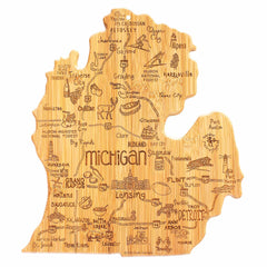 The Destination Michigan Mitten Cutting Board by Totally Bamboo, measuring 13-1/4" x 11-3/4", is intricately crafted from wood to beautifully represent the state of Michigan. It features laser-engraved artwork that highlights cities such as Detroit and Grand Rapids, along with landmarks like the Mackinac Bridge, while various symbols depict local culture and activities.