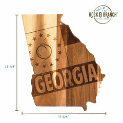 The Rock & Branch® Origins Series Georgia Cutting Board by Totally Bamboo is a state-shaped board made from acacia wood, boasting laser-engraved artwork of Georgia featuring a peach and stars in the upper left corner with "GEORGIA" across the middle. The board measures 13-1/4 inches tall by 11-3/4 inches wide and prominently displays the Rock & Branch logo in the top right.