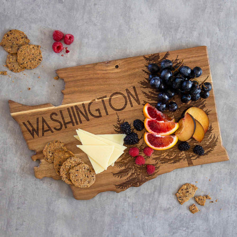 A Rock & Branch® Origins Series Washington Cutting Board from Totally Bamboo, crafted from acacia wood and featuring laser-engraved artwork with the word "Washington," is elegantly topped with sliced cheeses, crackers, blood oranges, plums, blackberries, raspberries, and grapes.