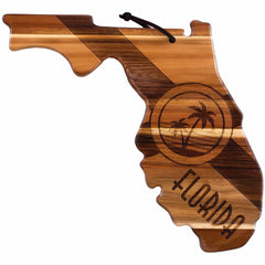 The Rock & Branch® Origins Series Florida Cutting Board by Totally Bamboo is an acacia wood board shaped like the state of Florida, showcasing a laser-engraved palm tree and the word "Florida." It combines light and dark wood tones with a leather loop for hanging, making it both a stunning and practical addition to your kitchen.