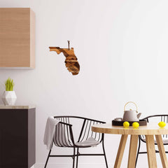 A modern, minimalistic kitchen showcases the Rock & Branch® Origins Series Florida Cutting Board by Totally Bamboo, featuring laser-engraved artwork of Florida on Acacia wood. The room is equipped with a wooden table adorned with a teapot and lemons, complemented by black chairs and geometric decor on the countertop against a white wall.