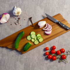 The Rock & Branch® Origins Series Tennessee Cutting Board by Totally Bamboo showcases sliced red onion, cucumber, and a kitchen knife. Whole cucumbers, garlic, peppercorns, and cherry tomatoes are artfully arranged around it on a gray surface. This striking piece also features laser-engraved artwork for an elegant touch.