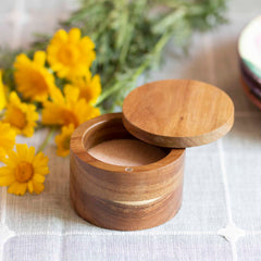 The Rock & Branch® Salt Cellar by Totally Bamboo, with its 6-oz. capacity and secure magnetic lock, is beautifully displayed on a textured tablecloth, surrounded by yellow flowers and greenery in the background.