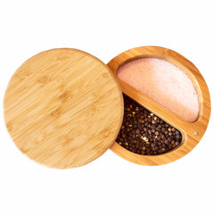 A round Totally Bamboo Salt Keeper Duet Salt Cellar with a magnetic lock has a lid that is slightly open, showcasing its contents. This stylish bamboo salt cellar is divided into two compartments, one containing coarse pink Himalayan salt and the other whole black peppercorns, making it ideal for any culinary enthusiast.