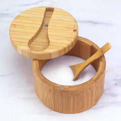 The Totally Bamboo Big Dipper Salt Cellar with Salt Spoon, featuring a 10-ounce capacity, is open to display the white salt within. A small bamboo spoon rests in the container. This elegant salt cellar sits on a white marble surface, highlighting its natural beauty and practicality.