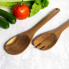 The Totally Bamboo TB Home® Acacia Wood Salad Serving Set, 12", elegantly crafted from acacia wood, rests on a light surface alongside fresh vegetables—tomato, lettuce leaves, and cucumbers—ready for your next delightful meal.