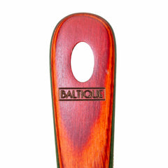 The image highlights the handle of the Totally Bamboo Baltique® Marrakesh Collection Slotted Spoon, 12-1/2", which features a smooth, oval hole near the top. The reddish-hued handle is engraved with "BALTIQUE" and is safe for use with non-stick cookware, making it versatile for various kitchen tasks.