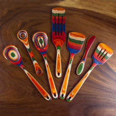 A 13-inch spurtle from the Baltique® Marrakesh Collection by Totally Bamboo, featuring seven wooden kitchen utensils with vibrant stripes and circular patterns in red, orange, green, and blue. Crafted from colored birch, these versatile tools are arranged fan-like on a wooden surface.