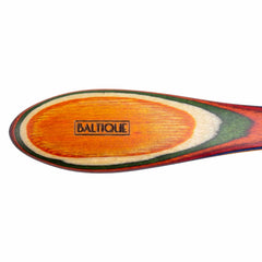 Close-up of a wooden spreader knife with vibrant, layered paint in orange, green, and white hues from the Totally Bamboo Baltique® Marrakesh Collection. The word "Baltique" is engraved in the center of the knife's surface.