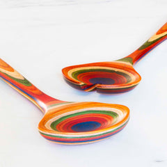 The Baltique® Marrakesh Collection Salad Serving Set by Totally Bamboo, measuring 11-3/4", rests on a white marble surface. Inspired by the vibrant marketplaces of Morocco, the set includes a spoon and fork, each featuring a distinctive multi-layered design in shades of red, orange, green, and blue.