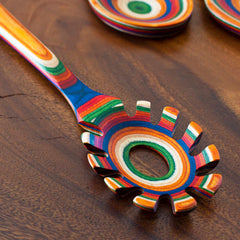 The Baltique® Marrakesh Collection Spaghetti Spoon by Totally Bamboo showcases a vibrant array of concentric rainbow rings on its wooden surface. Crafted from layered materials, including colored birch, this 12-1/2" spoon features a distinctive multicolored design with a round hole and prongs.