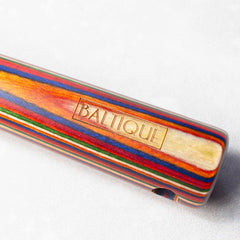 Close-up of a vibrant item crafted from colored birch, featuring the engraved text "BALTIQUE" from the Baltique® Marrakesh Collection Hawthorne Cocktail Strainer. The item showcases layered stripes in red, blue, yellow, and green against a light, neutral background. Proudly made by Totally Bamboo.