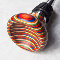 The Baltique® Marrakesh Collection Bottle Stopper by Totally Bamboo captures the essence of Morocco's vibrant marketplaces. This colorful accessory features a round, smooth top adorned with concentric rings in lively shades of red, blue, orange, yellow, and green. A silver metal neck paired with a black ribbed rubber section ensures it provides a snug seal.