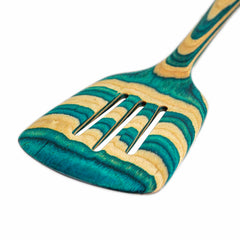 A detailed view of the Totally Bamboo Baltique® Mykonos Collection Slotted Spatula, 12-1/2", highlights its distinctive turquoise, blue, and natural wood grain design in colored birch. This lovely spatula includes three slots and a contoured handle.