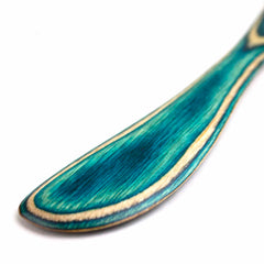 Close-up of a spreader knife with a smooth, curved handle from the Baltique® Mykonos Collection by Totally Bamboo. The knife showcases vibrant turquoise and colored birch patterns, creating a marbled effect. The image highlights the handle's intricate design.