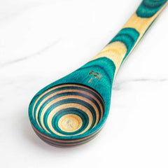 As a piece of the Baltique® Mykonos Collection by Totally Bamboo, this vibrant 2-in-1 measuring spoon is crafted from colored birch and showcases green and natural wood patterns. It is marked as 1 tablespoon and rests elegantly on a white marble surface.