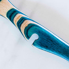 Close-up of the vibrantly carved handle of the Baltique® Mykonos Collection Notched Cooking Spoon by Totally Bamboo, showcasing an intricate design in shades of blue and natural wood tones against a grayish-white backdrop.