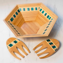 Hexagonal salad bowl from the Totally Bamboo Baltique® Mykonos Collection, highlighting teal and beige striped accents on durable bamboo, paired with a set of wooden salad servers featuring a matching inlay design, all displayed on a marble surface.