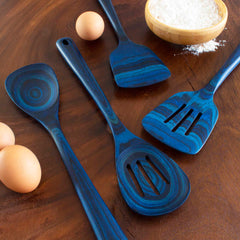 A set of four kitchen utensils in a blue marble pattern, featuring the Baltique® Malta Collection Slotted Spoon (12-1/2") by Totally Bamboo, along with a spatula and slotted spatula, is arranged on a wooden surface. Three brown eggs and a bowl of flour are placed around them.