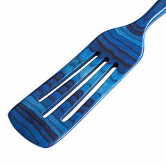 The Baltique® Malta Collection Spurtle by Totally Bamboo, measuring 13 inches, showcases a unique wavy striped pattern in blue on both the handle and head. This wooden kitchen spurtle, designed for use with non-stick cookware, features three elongated slots against a white background.