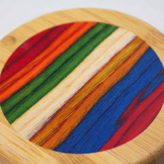 A circular salt cellar from the Baltique® Marrakesh Collection by Totally Bamboo, features vibrant, bold stripes in red, blue, orange, green, and natural wood tones. The vivid hues and natural wood grain create a striking contrast as it sits on a table.