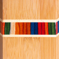 Close-up of a Moso bamboo surface with vibrant vertical stripes in red, blue, green, orange, and white, bordered by thin light wood bands. The texture and grain are clearly visible, resembling the kitchen utensil holder from the Baltique® Marrakesh Collection by Totally Bamboo.