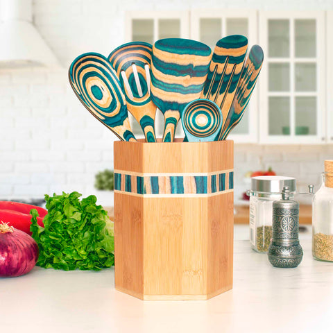 A set of vibrant wooden cooking utensils from the Baltique® Mykonos Collection by Totally Bamboo is tastefully displayed in a kitchen utensil holder made of Moso bamboo on the counter. Fresh lettuce, red onion, and an assortment of spices enhance the appeal of this bright and airy kitchen with its clean white cabinetry.