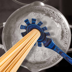 A blue spaghetti measuring tool, crafted from colored birch by Totally Bamboo, holds uncooked spaghetti over a pot of boiling water with bubbles forming on the surface. The scene captures the elegance synonymous with the Baltique® Malta Collection Spaghetti Spoon, 12-1/2", and complements your favorite non-stick cookware.