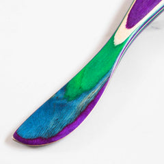 Close-up of the beautiful Baltique® Mumbai Collection Spreader Knife, 8" by Totally Bamboo, showcasing its handle adorned with colored birch in green, blue, purple, and natural wood hues. The artistic design stands out beautifully against the neutral background.