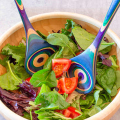 A wooden bowl brimming with a mixed greens salad, spotlighting sliced tomatoes, is complemented by two vibrant, spiral-patterned servers from the Totally Bamboo Baltique® Mumbai Collection Salad Serving Set, 11-3/4". The scene is set against a light, textured background.