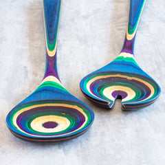 Introducing the Baltique® Mumbai Collection Salad Serving Set by Totally Bamboo, featuring two stunning wooden utensils adorned with lively, layered designs in blue, green, purple, and natural wood tones. Crafted from colored birch, these 11-3/4" utensils beautifully contrast against a light gray background.