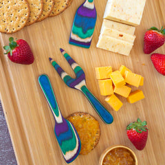 The wooden tray from the Baltique® Mumbai Collection 3-Piece Cheese Tool Set by Totally Bamboo showcases sliced cheese, round crackers, strawberries, and a dollop of marmalade on a cracker. The colored birch cheese knives included in the set add a vibrant touch to the arrangement.