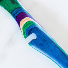 Close-up of the vibrant Baltique® Mumbai Collection Notched Cooking Spoon by Totally Bamboo, showcasing layered designs in blue, green, purple, and yellow on a light background reminiscent of colored birch patterns.