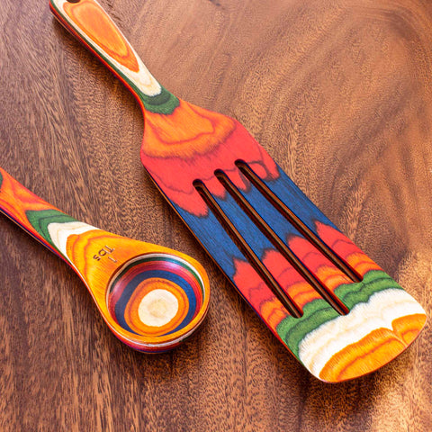 Totally Bamboo's Baltique® Marrakesh Collection 2-Piece Utensil Set includes a cooking spatula and a tablespoon measure, both embellished with vibrant rainbow stripes. Featuring shades of red, orange, blue, and green, these lively kitchen utensils are beautifully contrasted against their wooden surface.