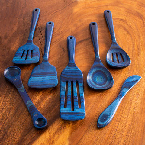 A 7-piece cooking utensil set from the Baltique® Malta Collection by Totally Bamboo, featuring blue and gray striped wooden spatulas, spoons, and a ladle displayed on a wooden surface. The unique stripe pattern and smooth texture showcase the craftsmanship of this elegant colored birch kitchen utensil set.