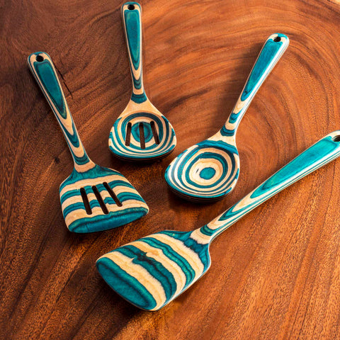 The Baltique® Mykonos Collection 4-Piece Cooking Utensil Set by Totally Bamboo features four elegantly designed blue and wood-striped kitchen tools, including a slotted spoon, ladle, spatula, and another distinctive slotted utensil, all beautifully complementing the wooden surface beneath.