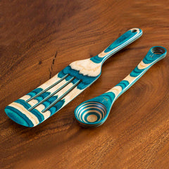 Explore the Baltique® Mykonos Collection by Totally Bamboo: a wooden utensil set featuring an eye-catching blend of teal and natural wood patterns on a rich brown wooden surface. This sophisticated 2-piece set includes a slotted spatula and a versatile spurtle, complemented by stackable 2-in-1 measuring spoons.