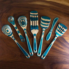 The Baltique® Mykonos Collection 7-Piece Cooking Utensil Set by Totally Bamboo presents a breathtaking display of intricate blue and natural woodgrain patterns. These colorful birch spoons and spatulas, each with its own unique swirling design, are elegantly arranged on a dark wooden surface.