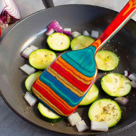 A pan filled with colorful vegetables and a vibrant Baltique® Montego Bay Collection Spatula, 12-1/2", crafted by Totally Bamboo from colored birch.