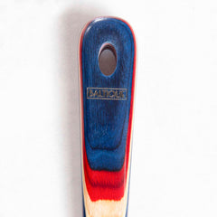 Close-up of a slotted spoon handle with a multicolored design in blue, red, and beige from the Baltique® Old Glory Collection by Totally Bamboo, featuring a small oval cutout near the top.