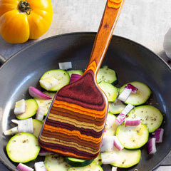 A Totally Bamboo Baltique® Poconos Collection Spatula, measuring 12-1/2 inches, rests in a frying pan alongside chopped zucchini and red onions, showcasing the rich hues of autumn. A yellow tomato is placed in the background.