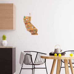 Modern kitchen with a round wooden table, two black chairs, and a teapot with lemons. A California Cutting Board with Artwork by Fish Kiss™, from the brand Totally Bamboo, hangs on a white wall. Minimalist decor, including wooden cabinets and a geometric plant holder, enhances the stylish setting.