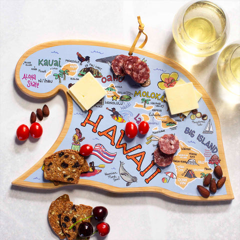 A Hawaiian Islands Cutting Board with Artwork by Fish Kiss™, crafted by Totally Bamboo, showcases a beautiful map of the islands and is adorned with cheese, salami, cherries, nuts, and crackers. Two glasses of white wine perfectly complement the bamboo cutting surface on a pristine white table.