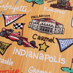 Discover the Indiana Cutting Board by Totally Bamboo, featuring artwork by Fish Kiss™. This vibrant and cartoonish design showcases Indiana locations like Lafayette and Kokomo, with playful elements. Indianapolis is spotlighted with a racing car and flag, while buildings and icons accentuate each city's name. A star marks Carmel in this charming illustration.