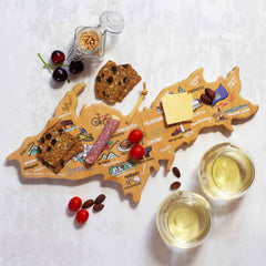 A Michigan Upper Peninsula Cutting Board with Artwork by Fish Kiss™, crafted by Totally Bamboo, elegantly displays crackers, cheese, and salami. Nearby, a pristine bamboo surface holds two glasses of white wine alongside cherries, grape tomatoes, and almonds.